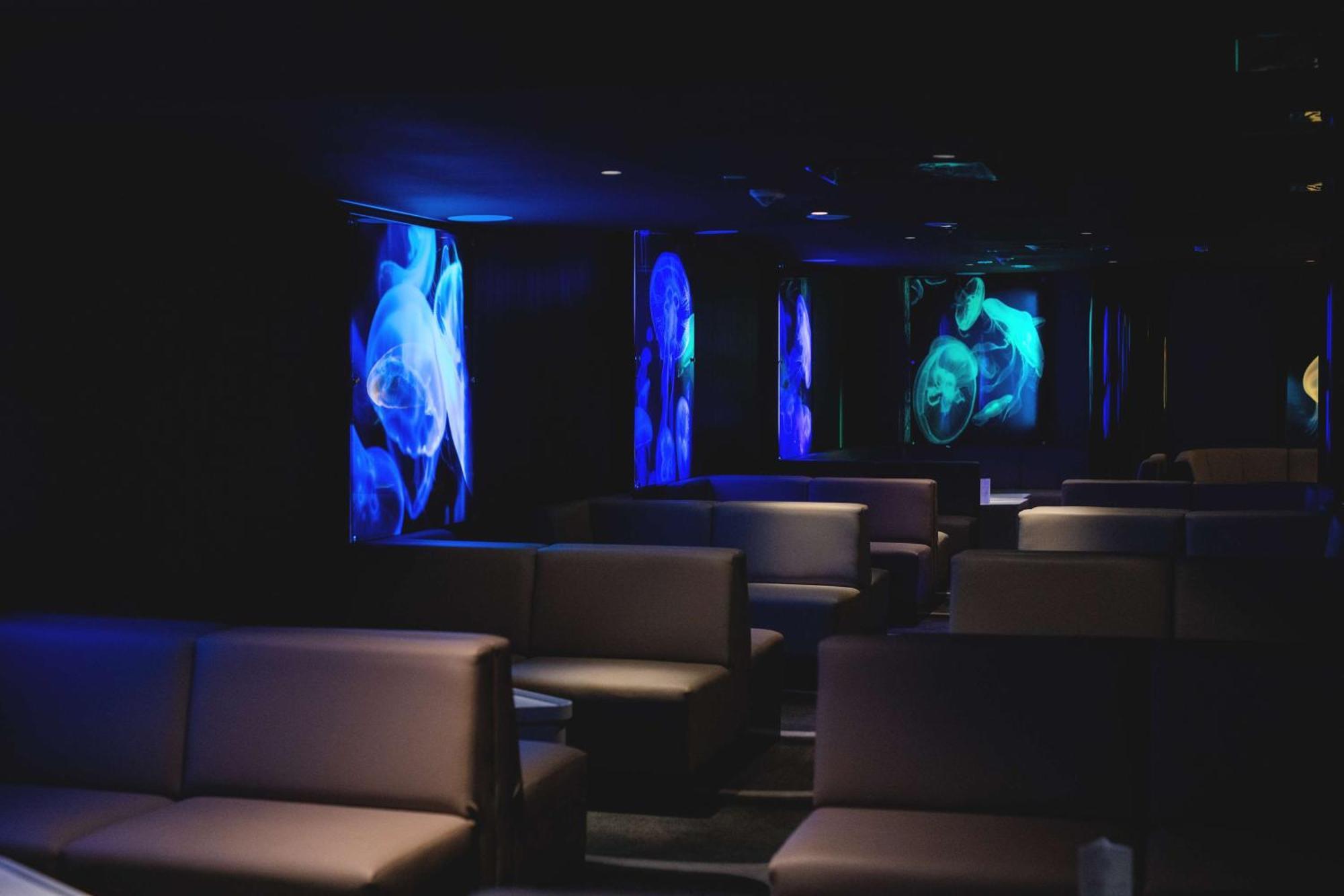 Radisson Blu Resort Swinoujscie Bagian luar foto The photo shows a dimly lit interior space, likely a lounge or a seating area. The walls are adorned with glowing blue and turquoise images, possibly of jellyfish or abstract aquatic forms, creating an ambient atmosphere. There are several upholstere