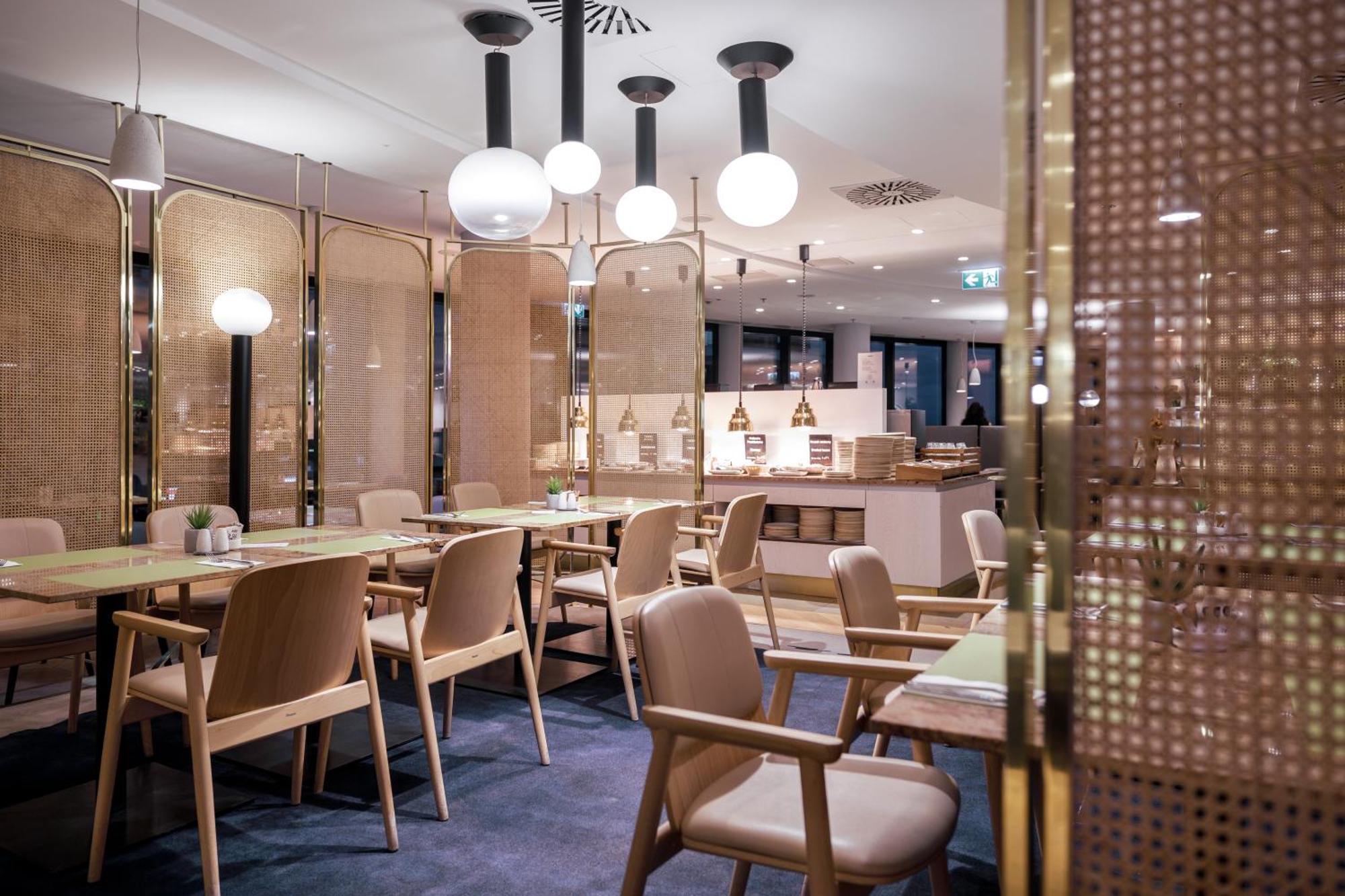 Radisson Blu Resort Swinoujscie Bagian luar foto The photo shows a modern restaurant interior. There are wooden tables and chairs arranged neatly. The atmosphere appears warm and inviting, with soft lighting provided by round pendant lamps hanging from the ceiling. Partitions made of woven material