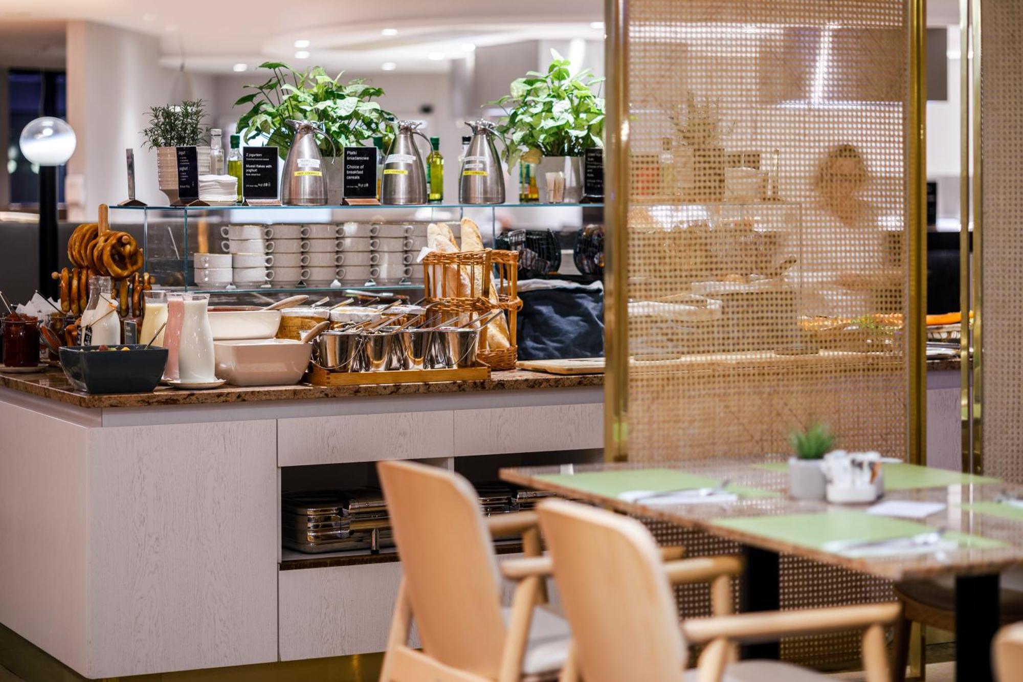 Radisson Blu Resort Swinoujscie Bagian luar foto The photo shows a modern café or dining area. In the foreground, there are wooden chairs and tables set up for dining. In the background, there is a display counter with various items, including plants in pots, containers, and possibly dishes or uten