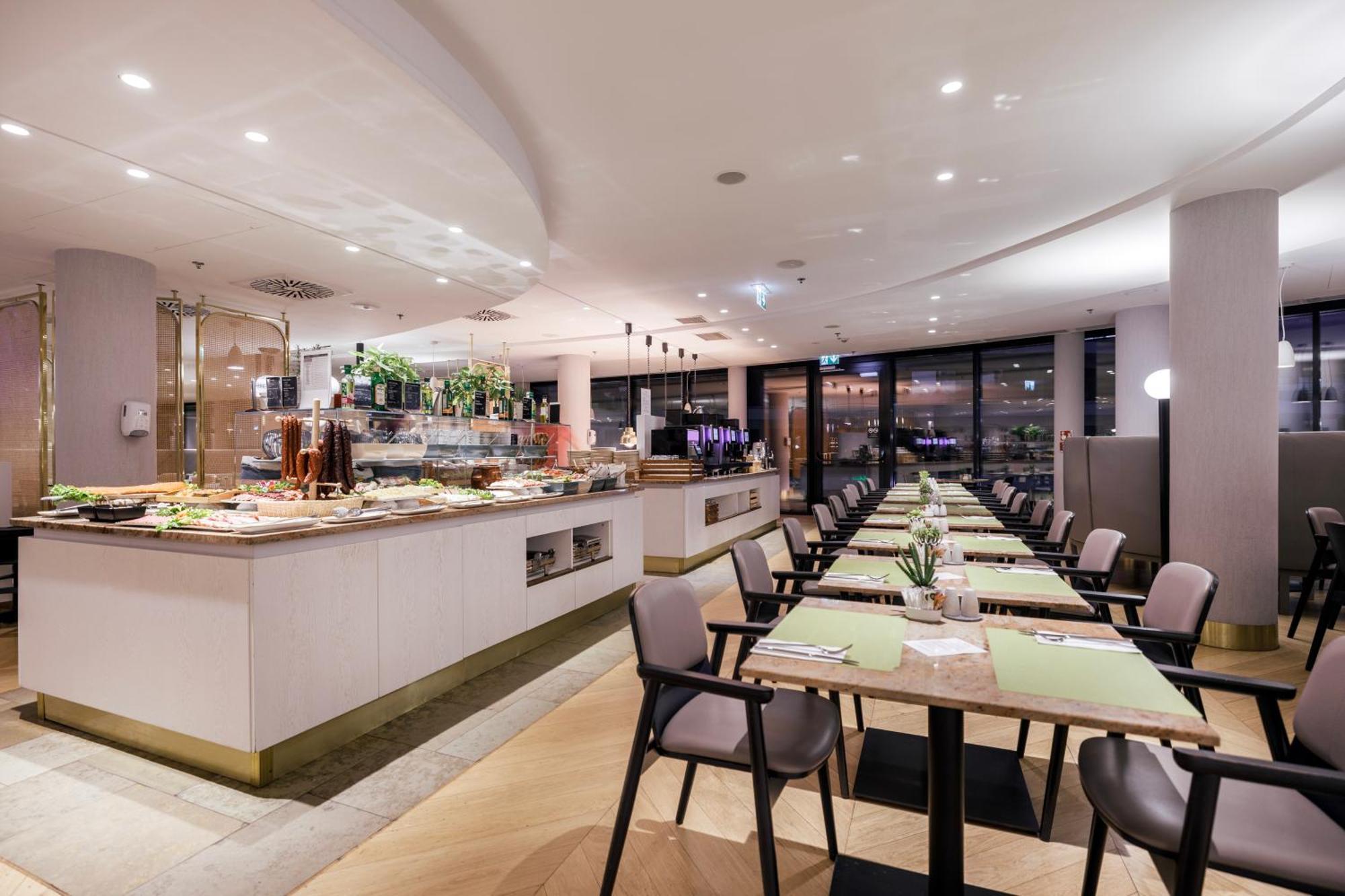 Radisson Blu Resort Swinoujscie Bagian luar foto The photo shows a modern restaurant interior. There is a long dining table set with green placemats, and several chairs arranged around it. To the left, there is a buffet area featuring a variety of dishes and drinks, beautifully presented. The resta