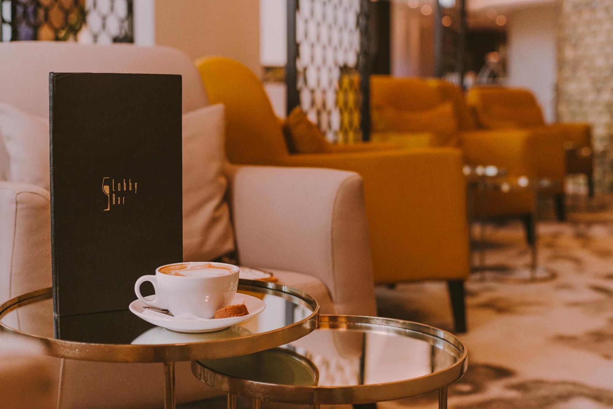 Radisson Blu Resort Swinoujscie Bagian luar foto The photo shows a cozy indoor setting with a stylish, modern atmosphere. In the foreground, there is a small round glass table with a white coffee cup and a saucer, alongside a small biscuit or cookie. Next to the coffee, there is a black menu with e