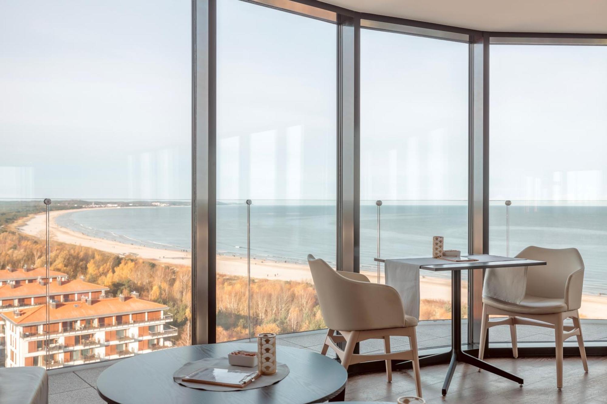 Radisson Blu Resort Swinoujscie Bagian luar foto The photo shows a modern interior space with large floor-to-ceiling windows that provide a stunning view of the beach and sea. The area appears to be a dining or lounge space, featuring a minimalistic table and chairs. There is a sense of tranquility