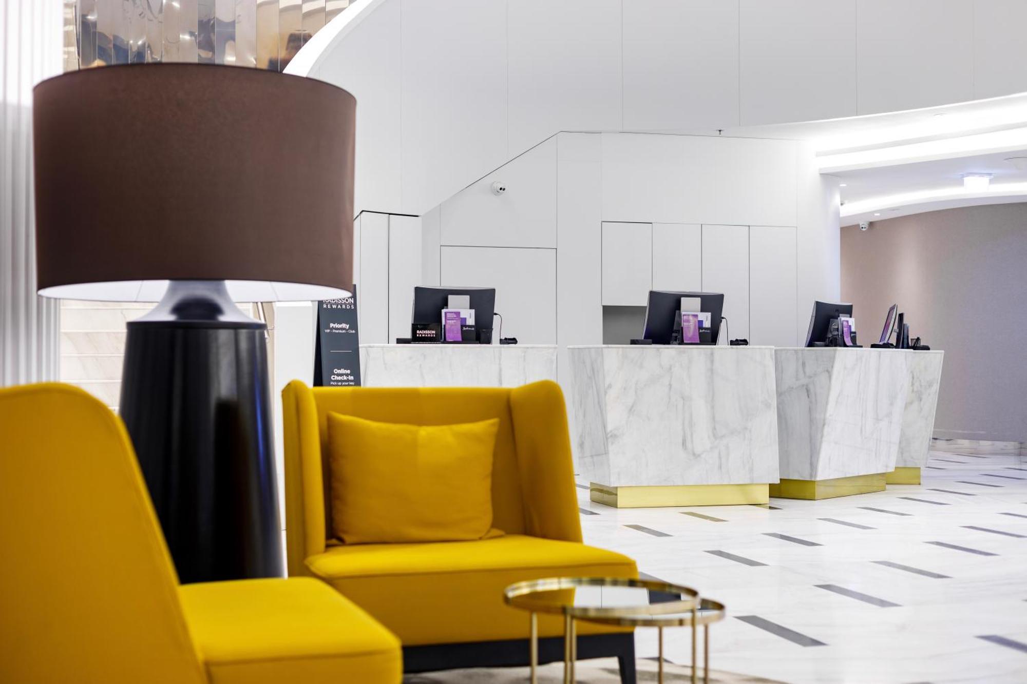 Radisson Blu Resort Swinoujscie Bagian luar foto The photo shows a modern reception area, likely of a hotel or a similar establishment. In the foreground, there are two yellow armchairs with soft cushions, situated around a small round table with a minimalist design. Behind the seating area, there 