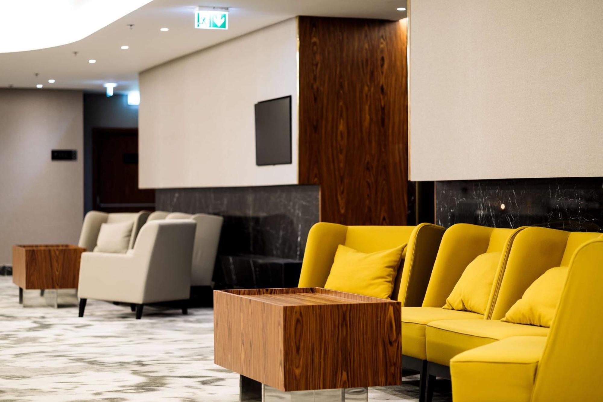 Radisson Blu Resort Swinoujscie Bagian luar foto The photo depicts a modern lounge or waiting area with stylish seating. On the left, there are soft gray armchairs arranged around a wooden coffee table. In the center, there are yellow chairs with plush cushions, contributing a vibrant contrast to t