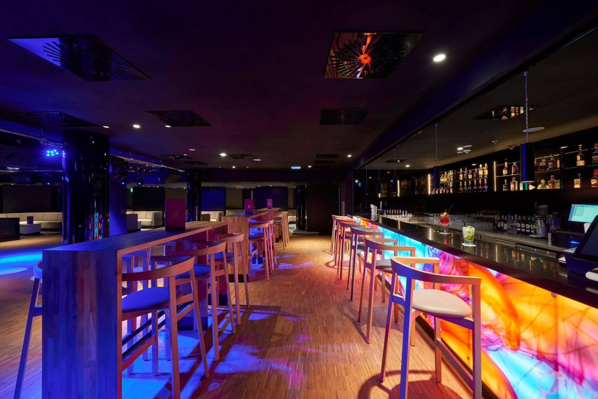 Radisson Blu Resort Swinoujscie Bagian luar foto The photo depicts a modern bar interior with a sleek and contemporary design. There are high wooden stools positioned along a bar counter, which features vibrant, colorful lighting underneath. The bar area is dimly lit, creating a nightlife ambiance,