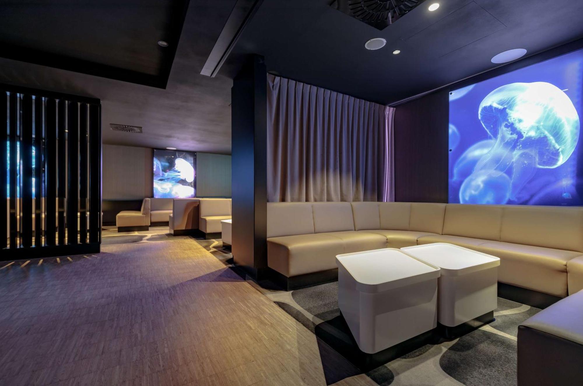 Radisson Blu Resort Swinoujscie Bagian luar foto The photo shows a modern interior space that appears to be a lounge or relaxation area. The design is sleek and minimalist, featuring a curved, light-colored seating arrangement with low tables at the center. The walls are dark, contributing to a coz