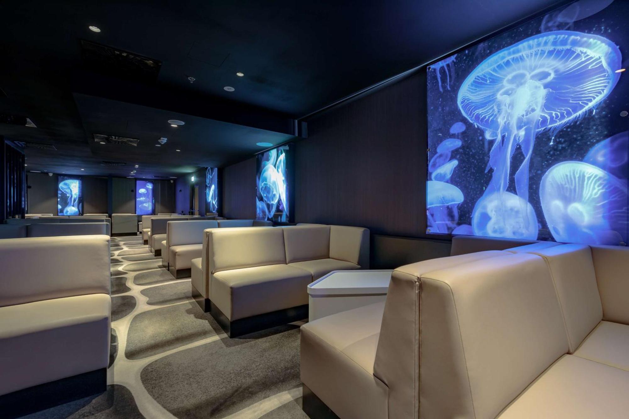 Radisson Blu Resort Swinoujscie Bagian luar foto The photo shows a modern lounge space with a sleek design. The area features light-colored, upholstered seating arranged in an open layout. The walls are decorated with large, vibrant images of jellyfish illuminated in blue, creating a calming underw