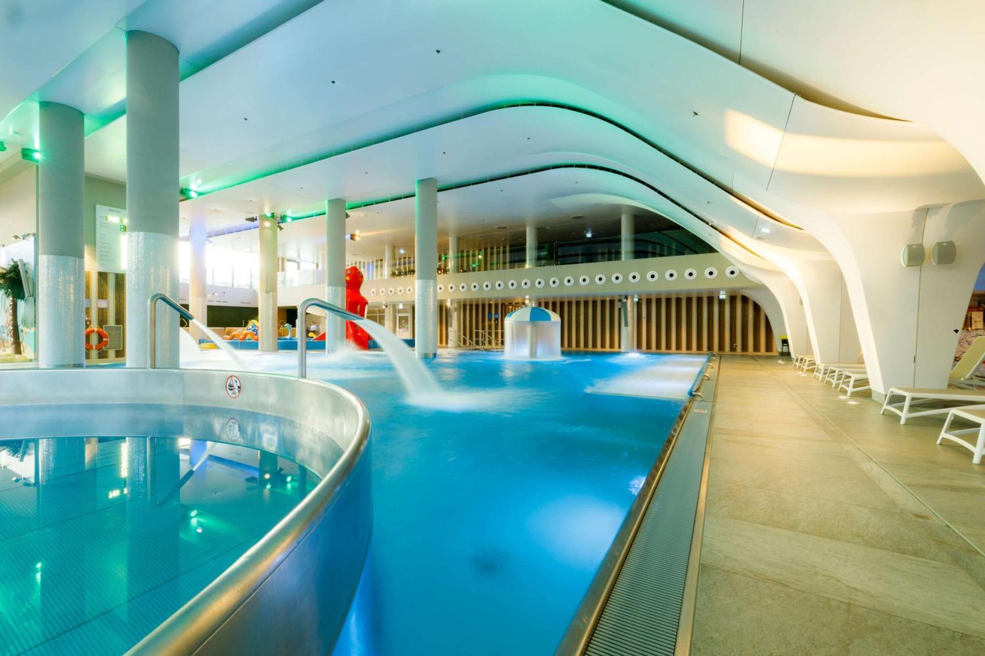 Radisson Blu Resort Swinoujscie Bagian luar foto The photo shows a modern indoor swimming pool area with an elegant design. The pool features curved edges and is filled with clear, blue water. There are various amenities, such as jets for relaxation and possibly seating areas along the edges. The l