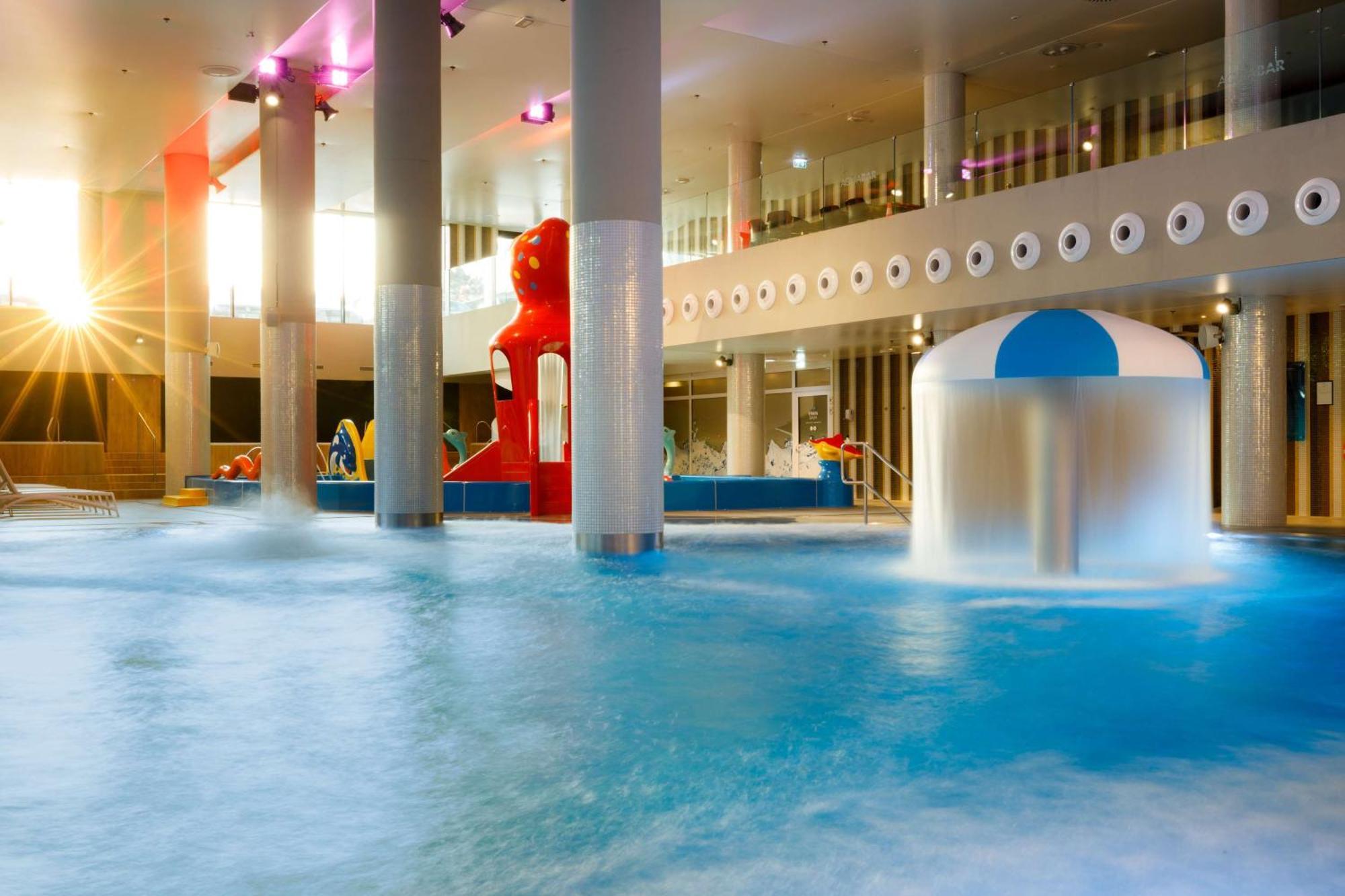 Radisson Blu Resort Swinoujscie Bagian luar foto The photo shows an indoor water park or pool area. There is a large body of water with playful features, including a water slide shaped like a red bear and a smaller structure with a blue and white canopy. The lighting is bright, suggesting a sunny a