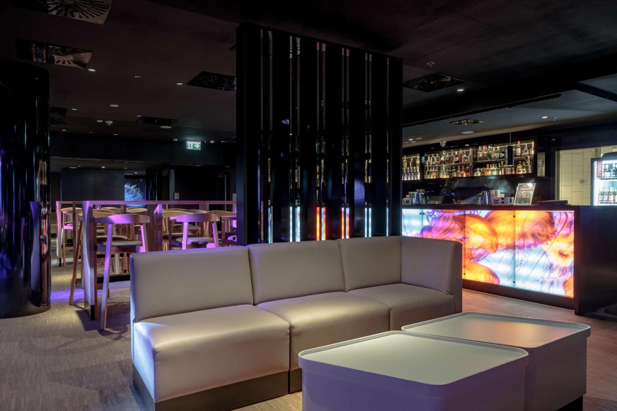 Radisson Blu Resort Swinoujscie Bagian luar foto The photo depicts a modern interior space, possibly a lounge or bar. There are sleek, minimalistic furniture pieces, including a large, curved sofa and contemporary coffee tables. The lighting is dim, with a blend of colorful ambient lights illuminat