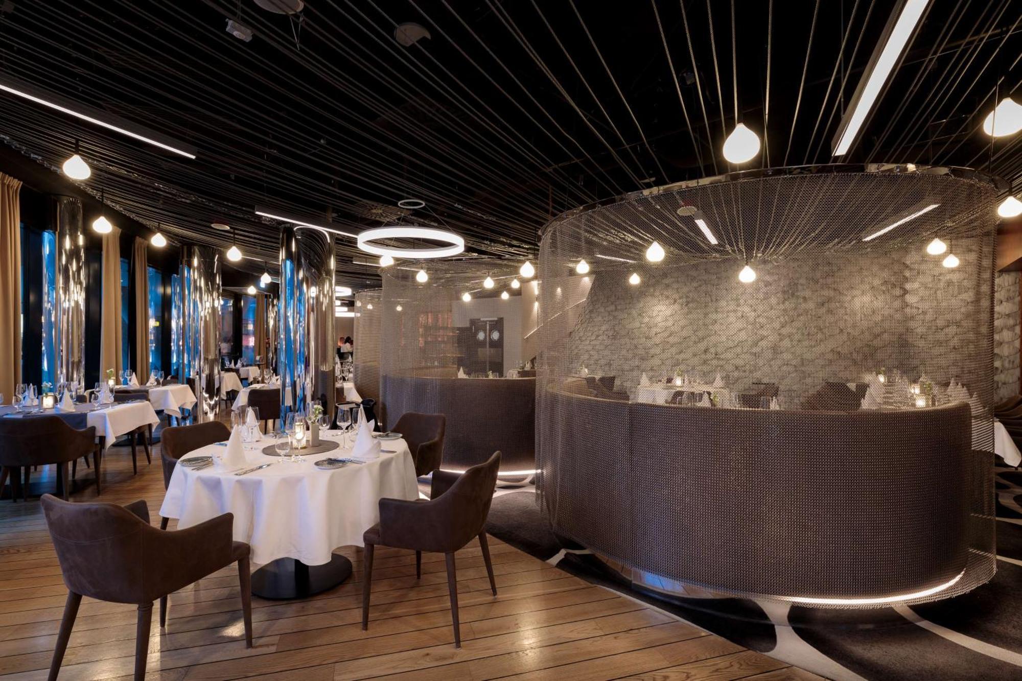 Radisson Blu Resort Swinoujscie Bagian luar foto The photo shows an elegant restaurant interior. It features polished wooden floors and contemporary decor. Round tables are set with white tablecloths and have chairs arranged around them. The lighting is modern, with multiple pendant lights hanging 