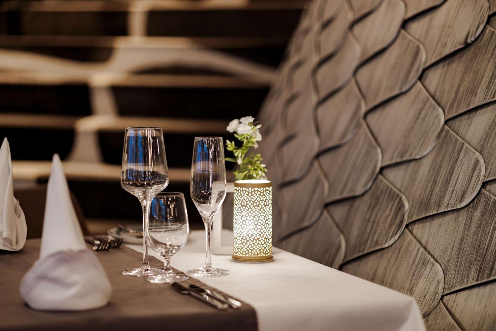 Radisson Blu Resort Swinoujscie Bagian luar foto The photo shows a beautifully arranged table setting in a restaurant. There are two elegant wine glasses and a smaller glass, likely for water, placed on a crisp white tablecloth. A decorative lantern with intricate designs holds a small flower arran