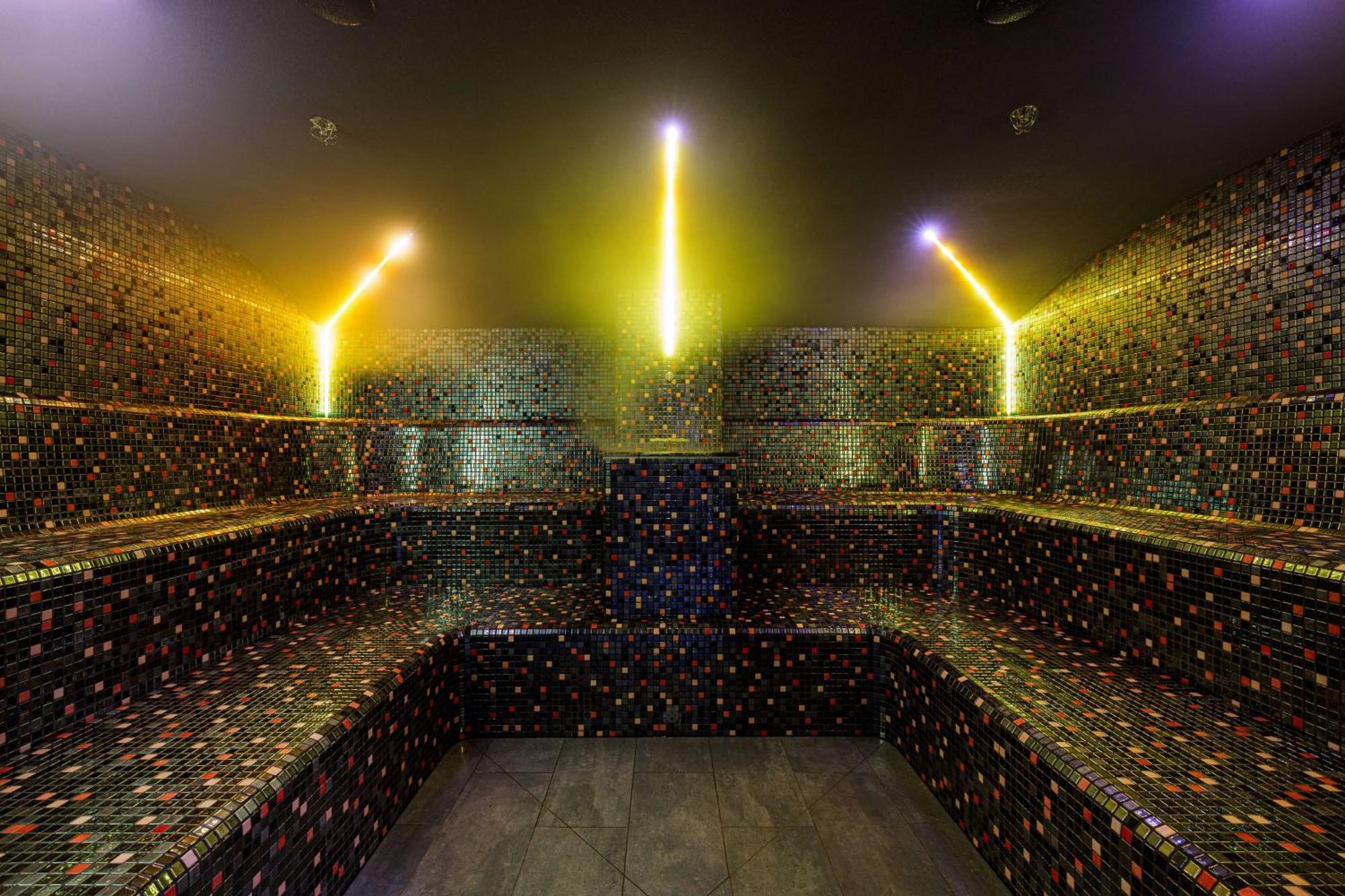 Radisson Blu Resort Swinoujscie Bagian luar foto The photo shows the interior of a steam room or sauna. The space is characterized by a series of benches that are built into the walls, allowing for multiple seating options. The walls are adorned with a mosaic of small, colorful tiles that create a 