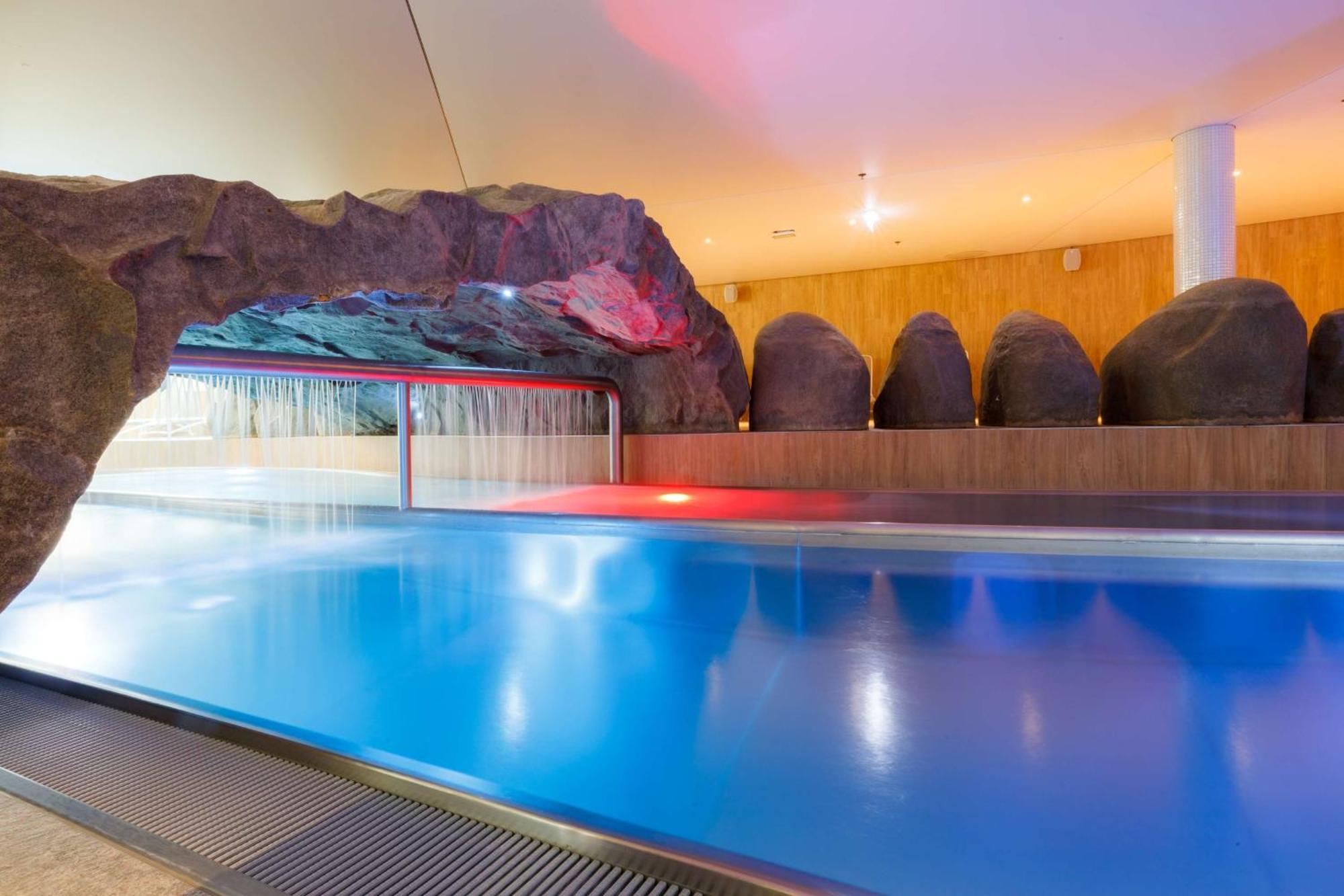 Radisson Blu Resort Swinoujscie Bagian luar foto The photo shows a serene indoor swimming pool area. The pool has clear blue water, and there is a distinctive rock formation that resembles a cave on one side. Soft lighting enhances the atmosphere, casting a gentle glow across the space. In the back