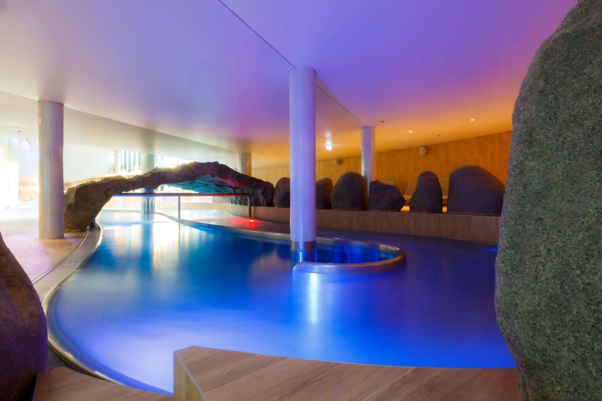 Radisson Blu Resort Swinoujscie Bagian luar foto The photo showcases an elegant indoor swimming pool area. The pool has a flowing, organic shape and is illuminated with soft blue and purple lighting, creating a calming ambiance. Surrounding the pool are smooth, natural-looking stones and wooden ele
