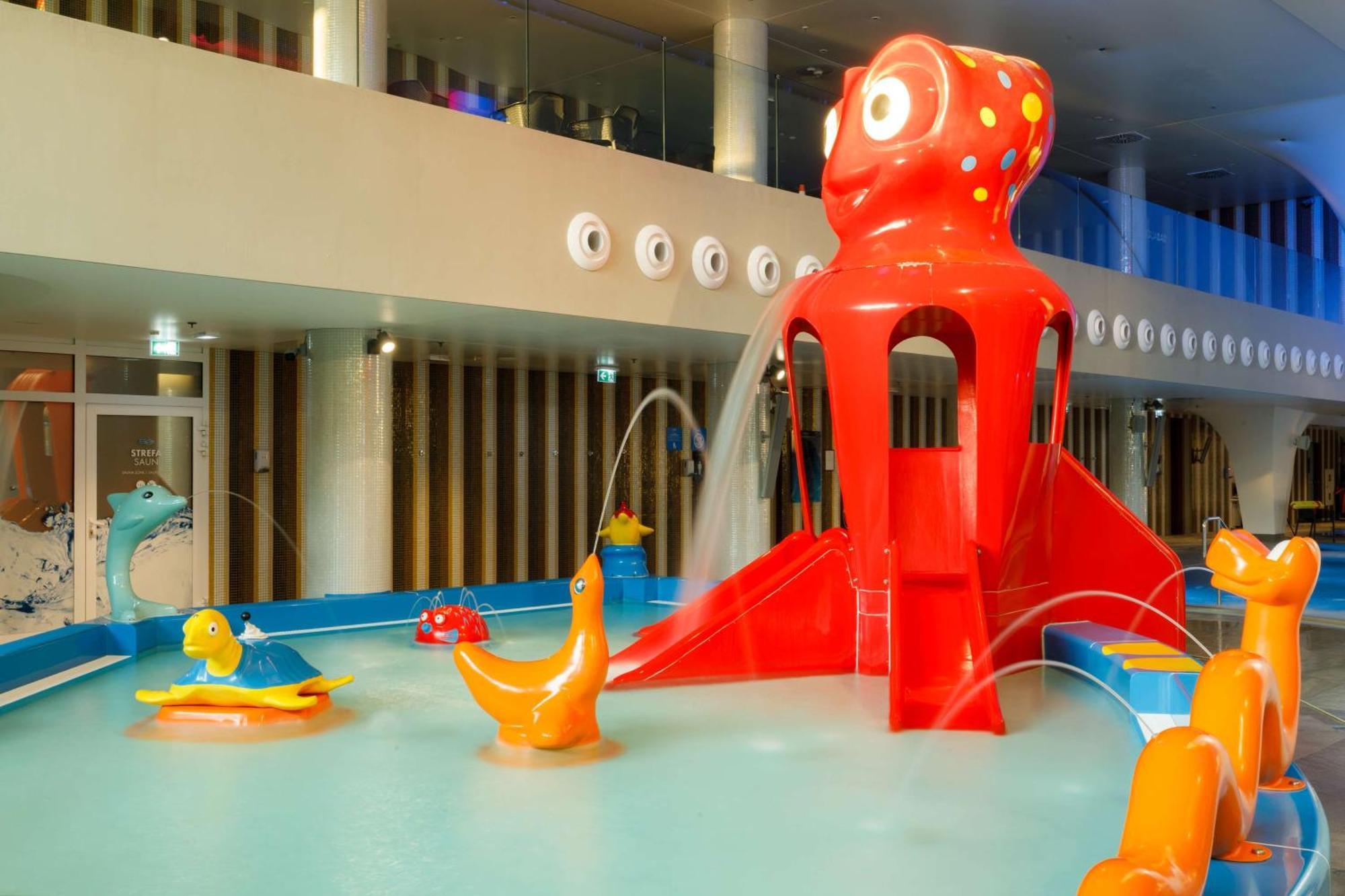Radisson Blu Resort Swinoujscie Bagian luar foto The photo shows a colorful indoor splash pad or water play area designed for children. Central to the scene is a large, bright red octopus structure, which has water fountains spraying out. Surrounding it are various playful, colorful water animals, 